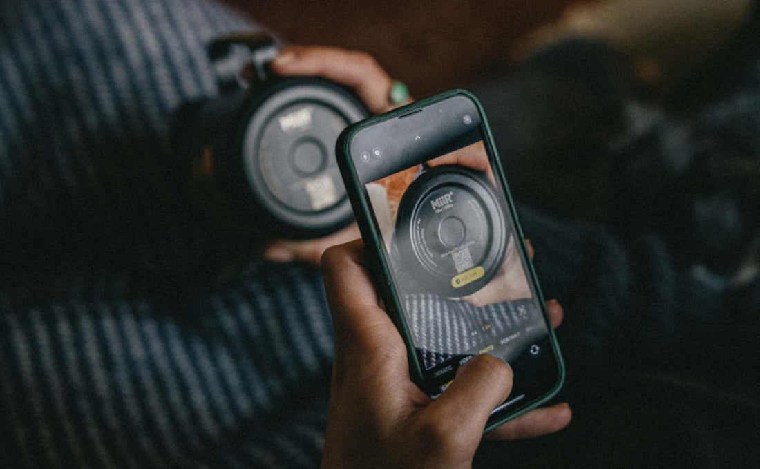 A bottle, bearing a QR code on the bottom being scanned by a smartphone.